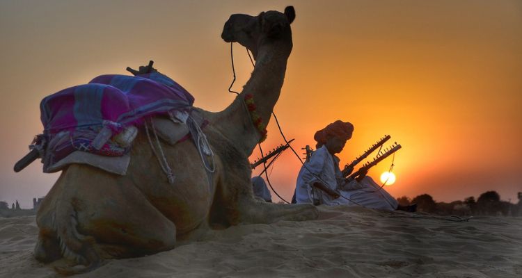 Traditional camel herder in Rajasthan desert at sunset.